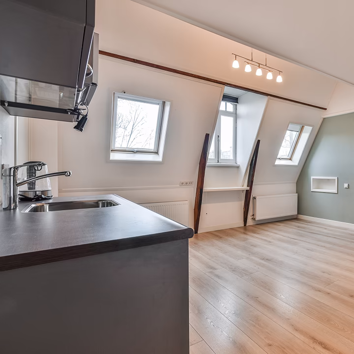 Jasny aneks kuchenny na poddaszu z ciemnym blatem i oknami.