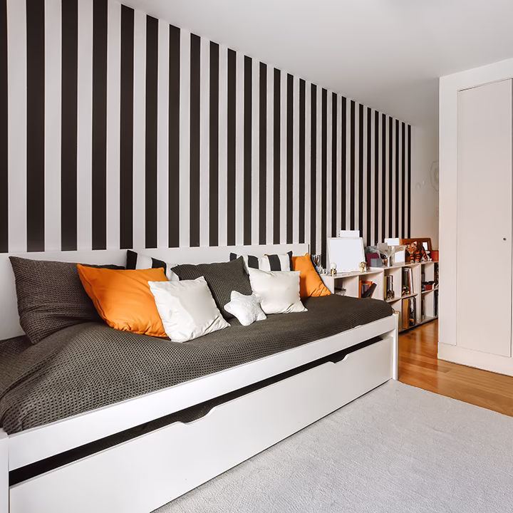 Białe łóżko w pokoju z czarno-białą tapetą w pasy.