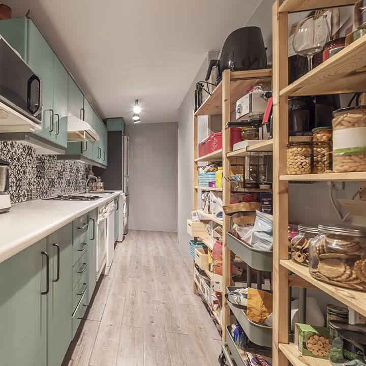 Wąska kuchnia z miętowymi szafkami i drewnianymi regałami spiżarnianymi.
