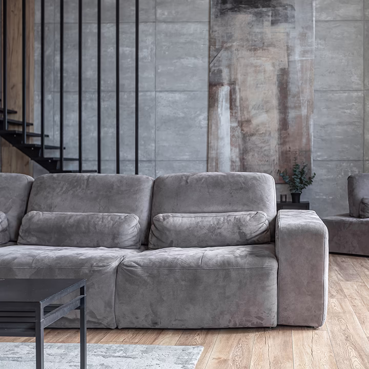 Nowoczesny salon z szarą sofą, betonowymi ścianami i drewnianą podłogą.